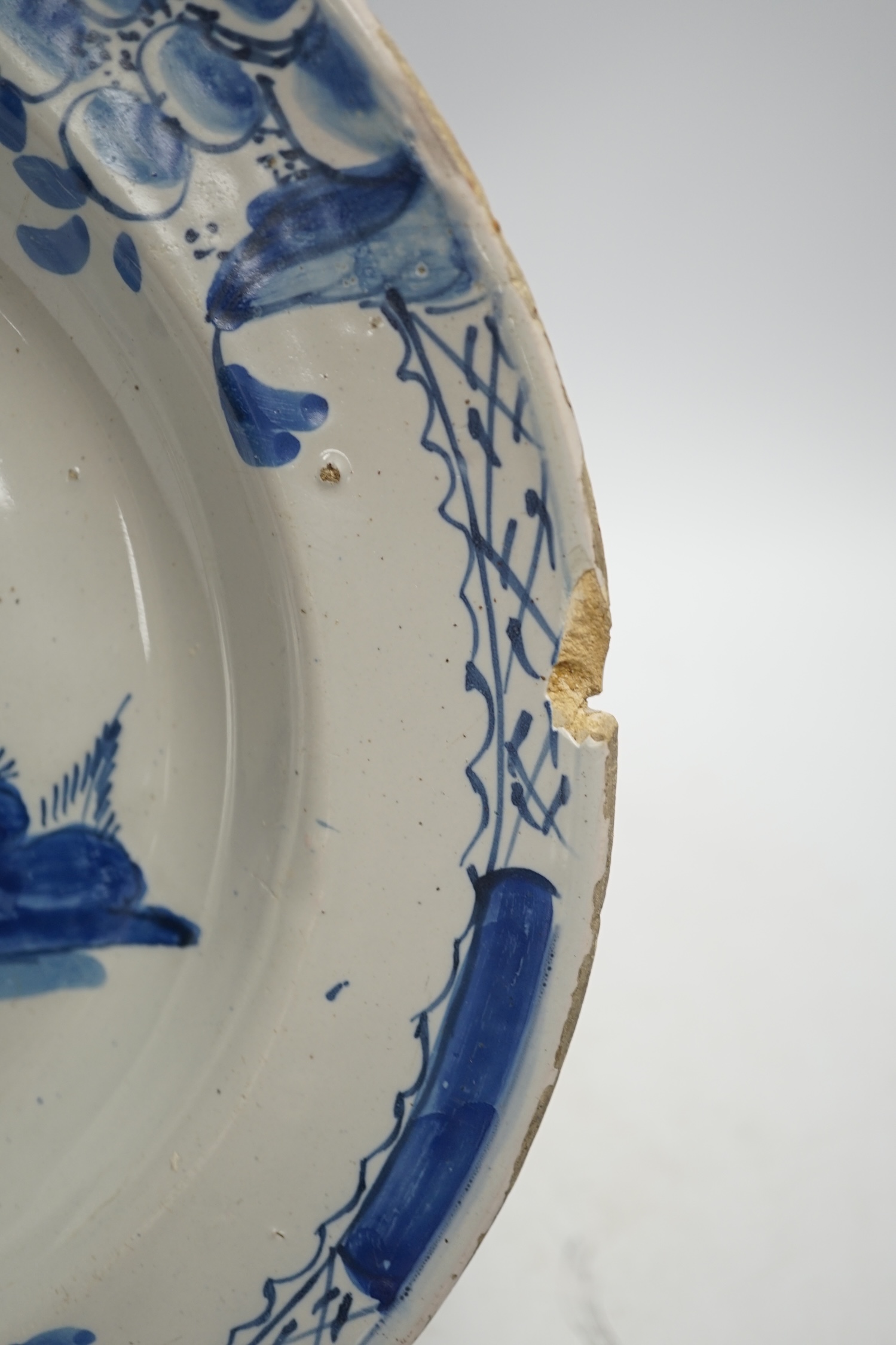 An 18th century Delft dish, decorated with a Chinese scene of a figure with a parasol, diameter 28cm. Condition - damaged to rim